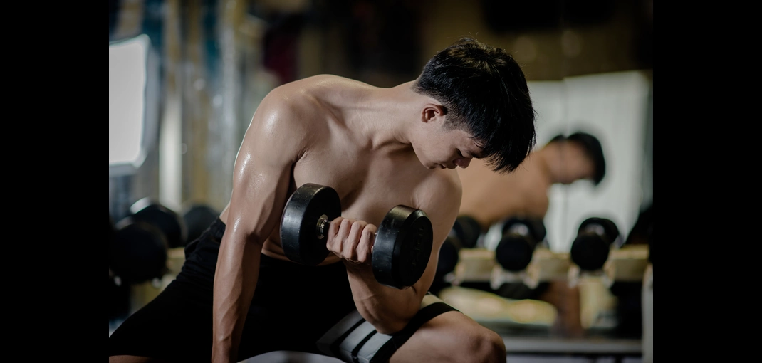 Pria angkat beban saat latihan gym untuk menggambarkan pentingnya kebutuhan protein harian gym dalam membangun otot